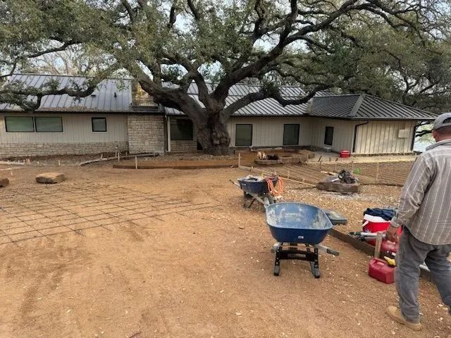 Construction site: House with large tree, worker, wheelbarrows, and rebar.