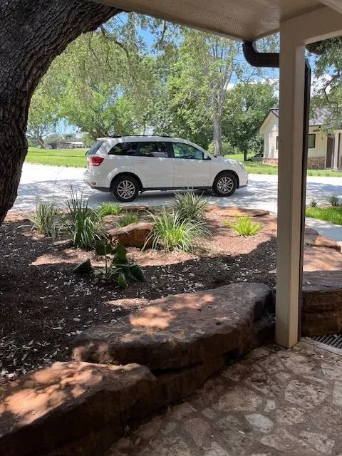 White SUV parked on a driveway near a house. Landscaping and a tree are in the foreground.