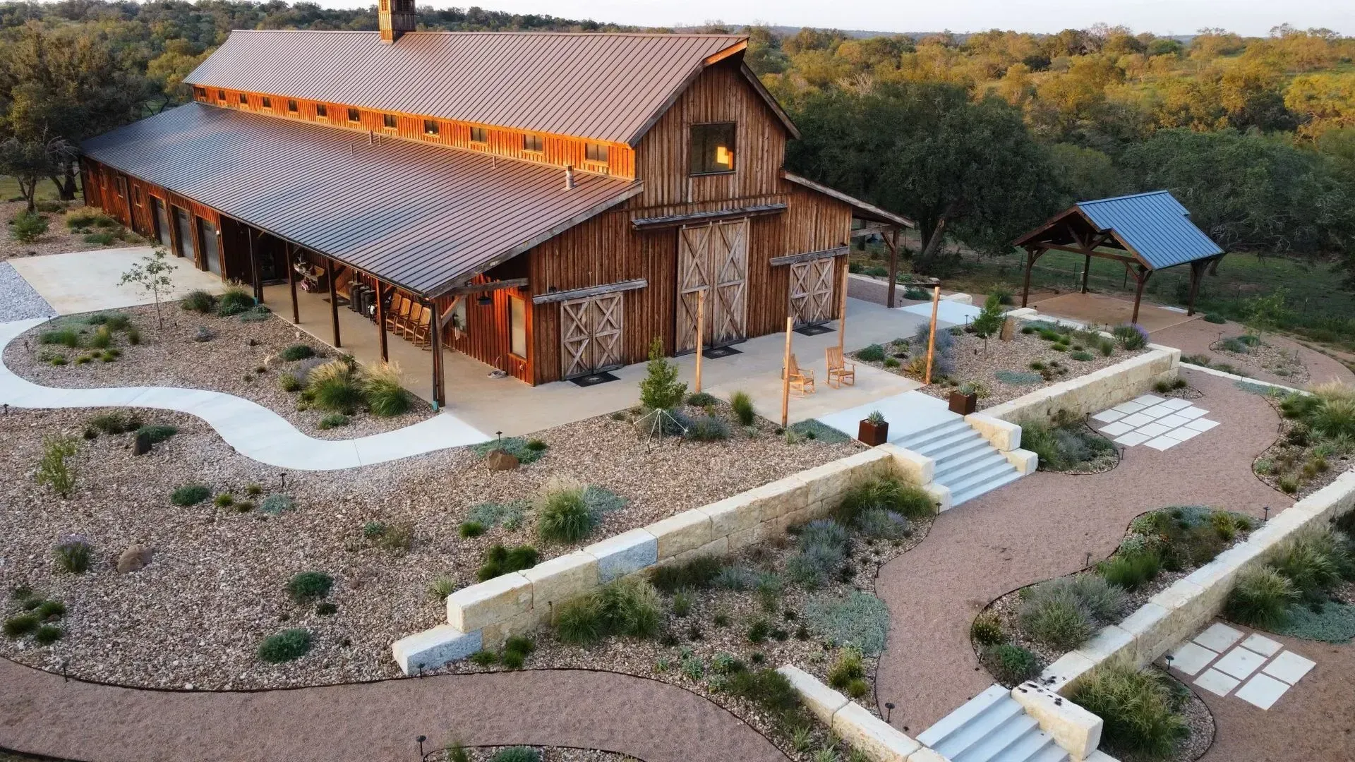 Rustic wooden barn with a metal roof surrounded by landscaping and stone pathways.