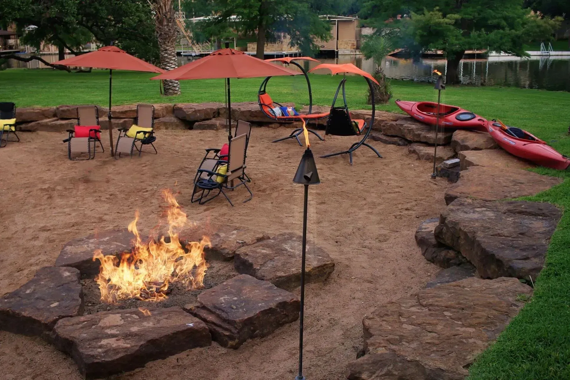 Fire pit area with a sandy ground, chairs, umbrellas, and kayaks.
