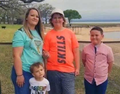 Four people posing outdoors: a woman, two youths, and a toddler. The woman wears teal, the youth in orange.