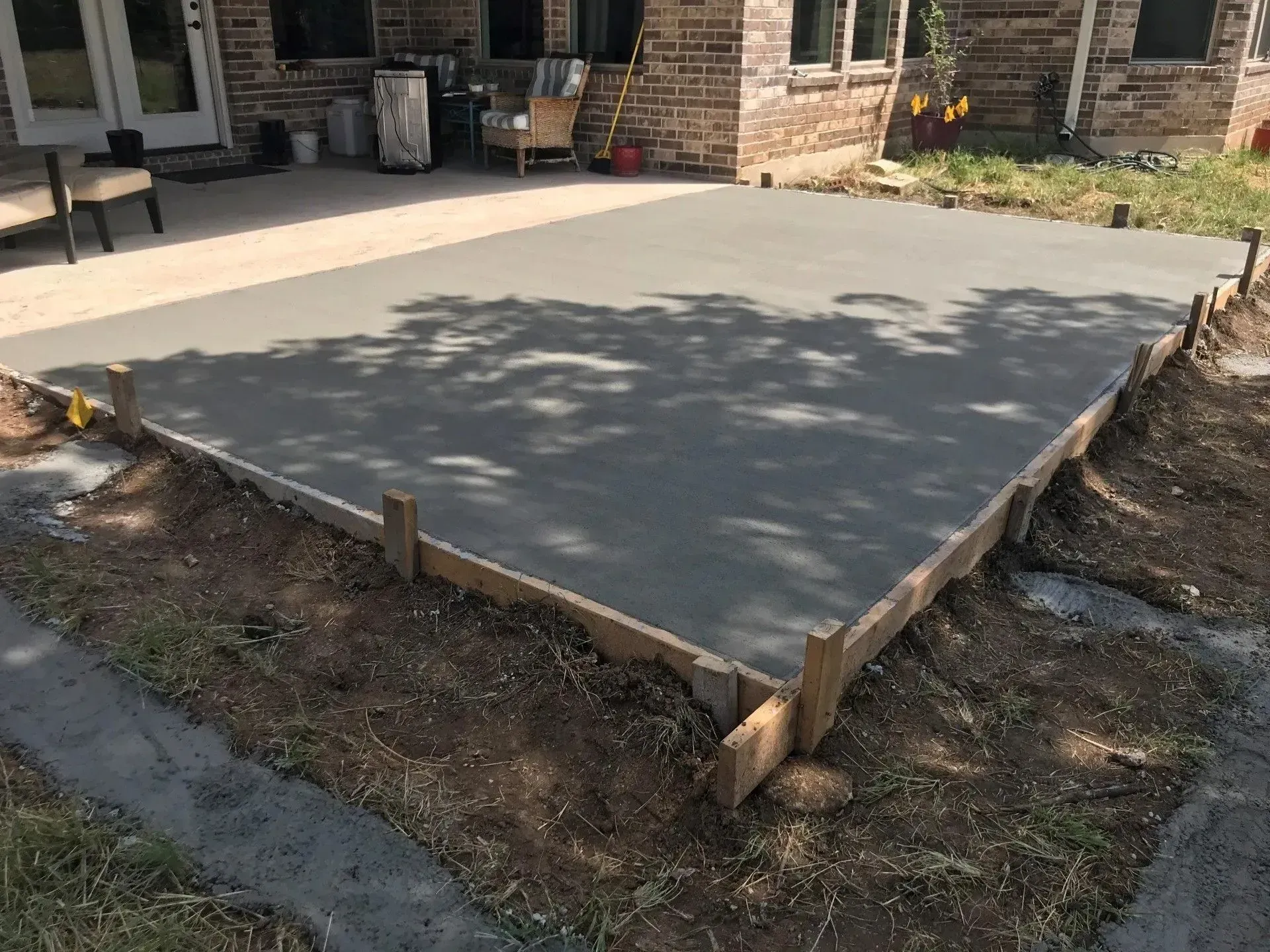 Freshly poured concrete patio surrounded by wooden forms, near a house and grassy area.