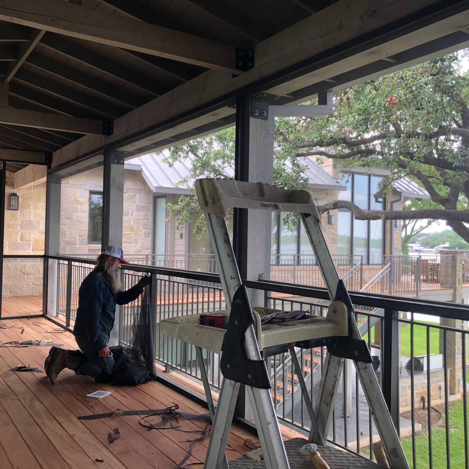 Person installing screen on porch with a ladder, overlooking a lake and home.