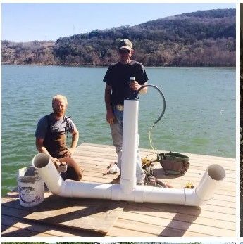 Two men on a dock with a PVC pipe structure near a lake, one holds a tube, the other kneels.