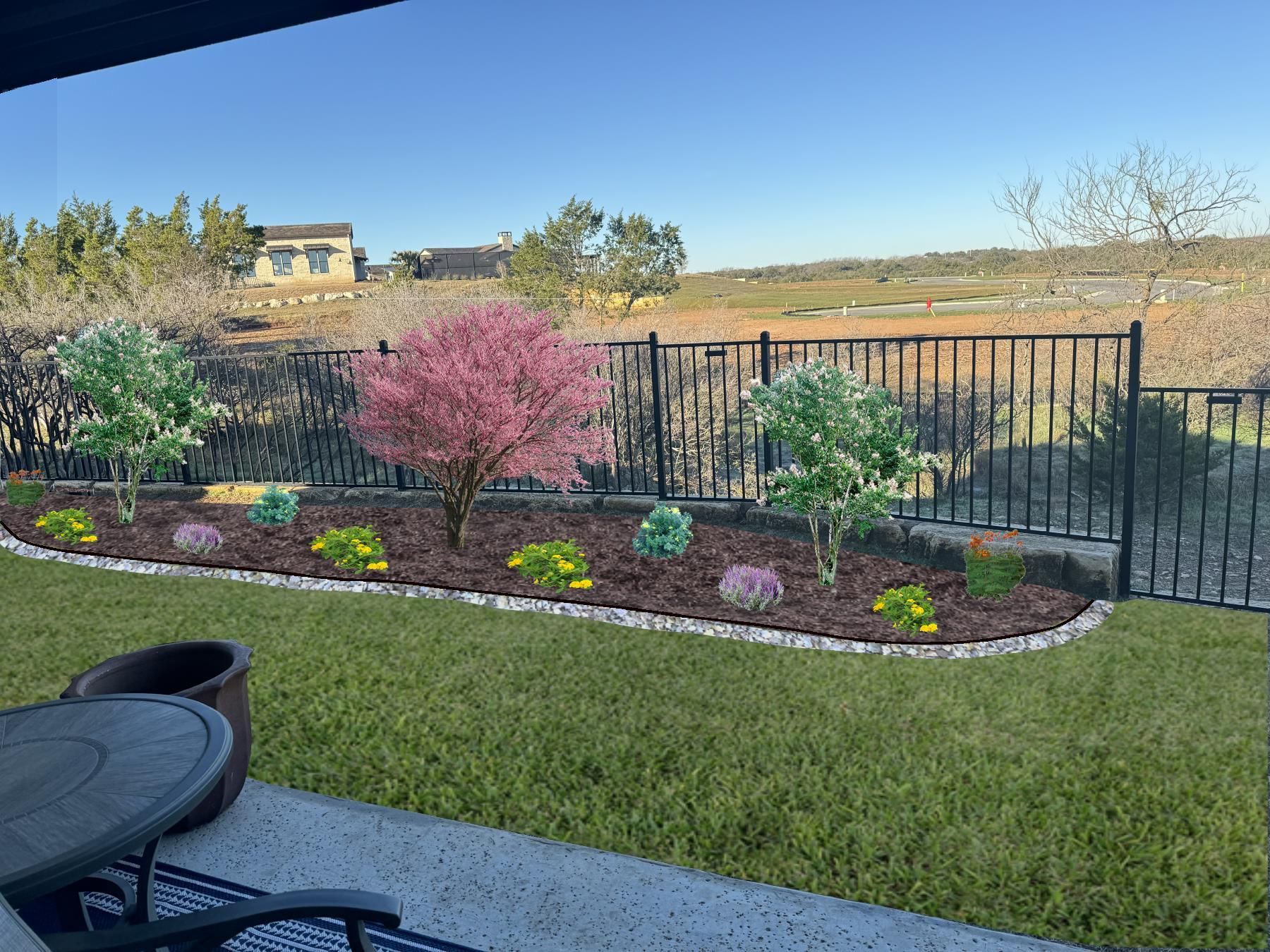 Landscaped garden bed with flowering trees and bushes, outlined by a black fence and a grassy yard.