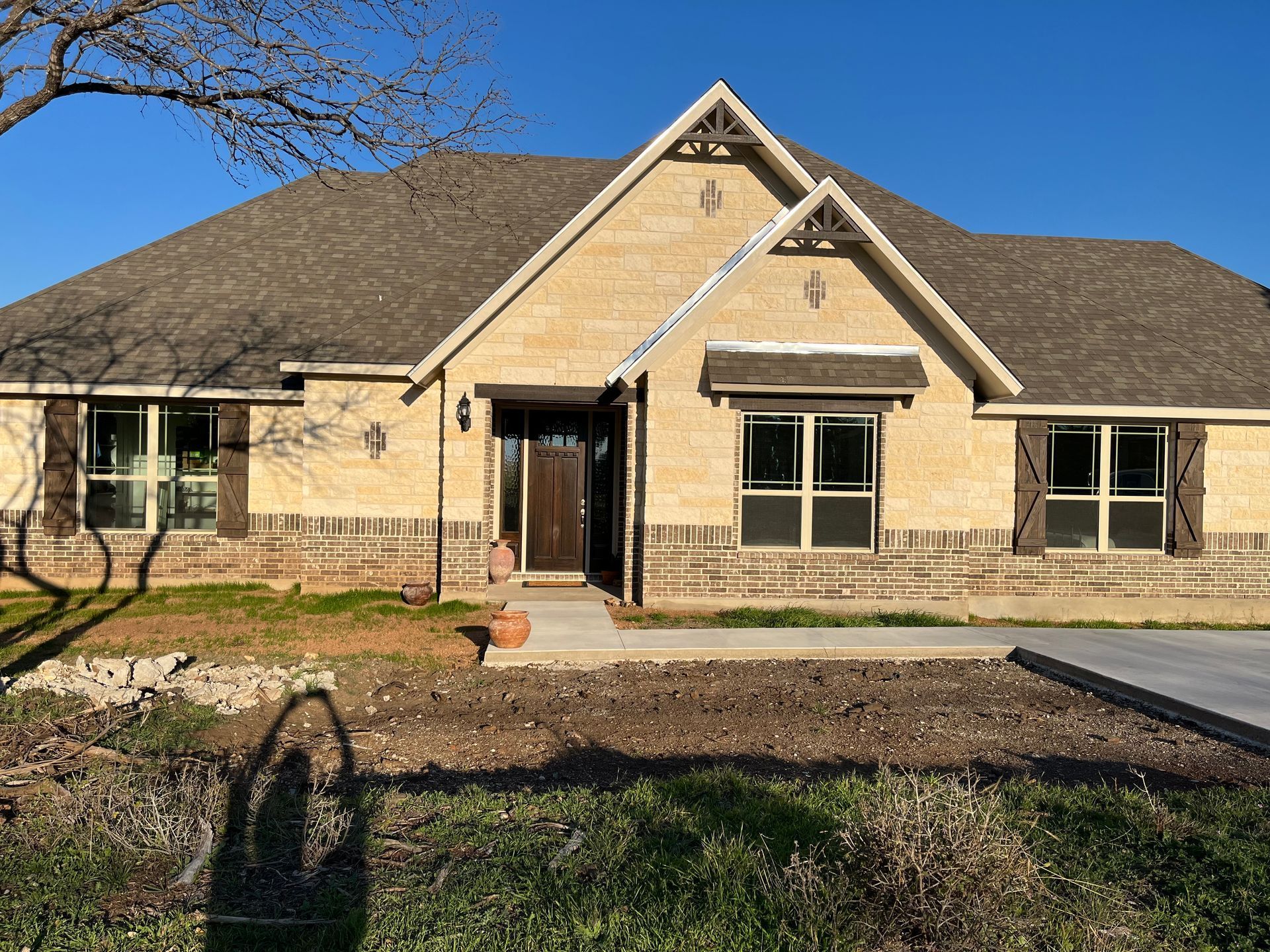 Tan brick house with brown roof and trim against a clear blue sky.