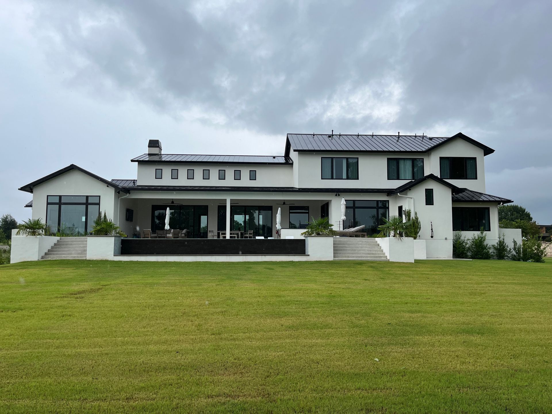 Back view of a large, two-story white house with black trim and a dark gray roof on a grassy lawn.