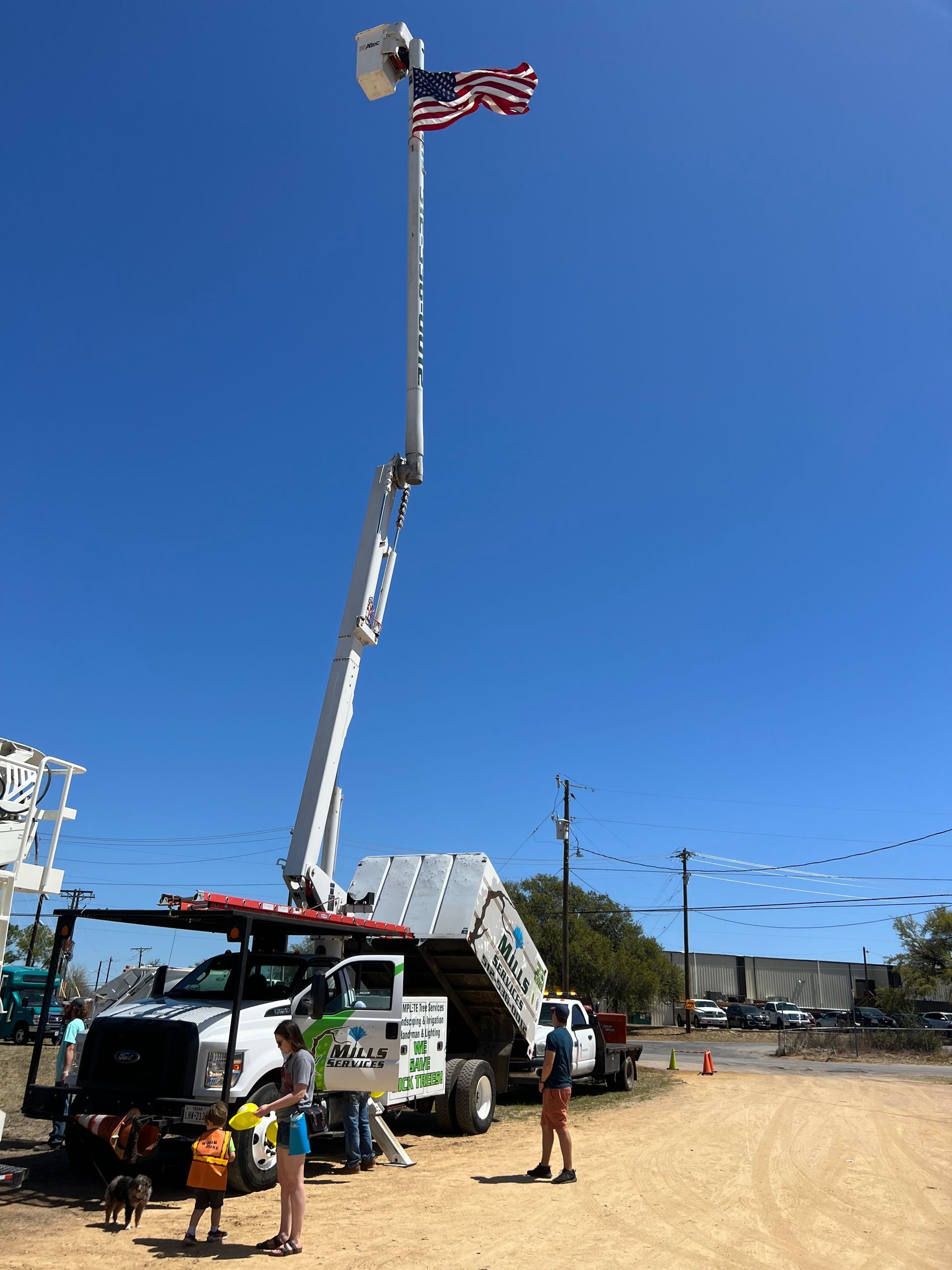 Bucket truck displaying US flag; people on ground, sunny day.