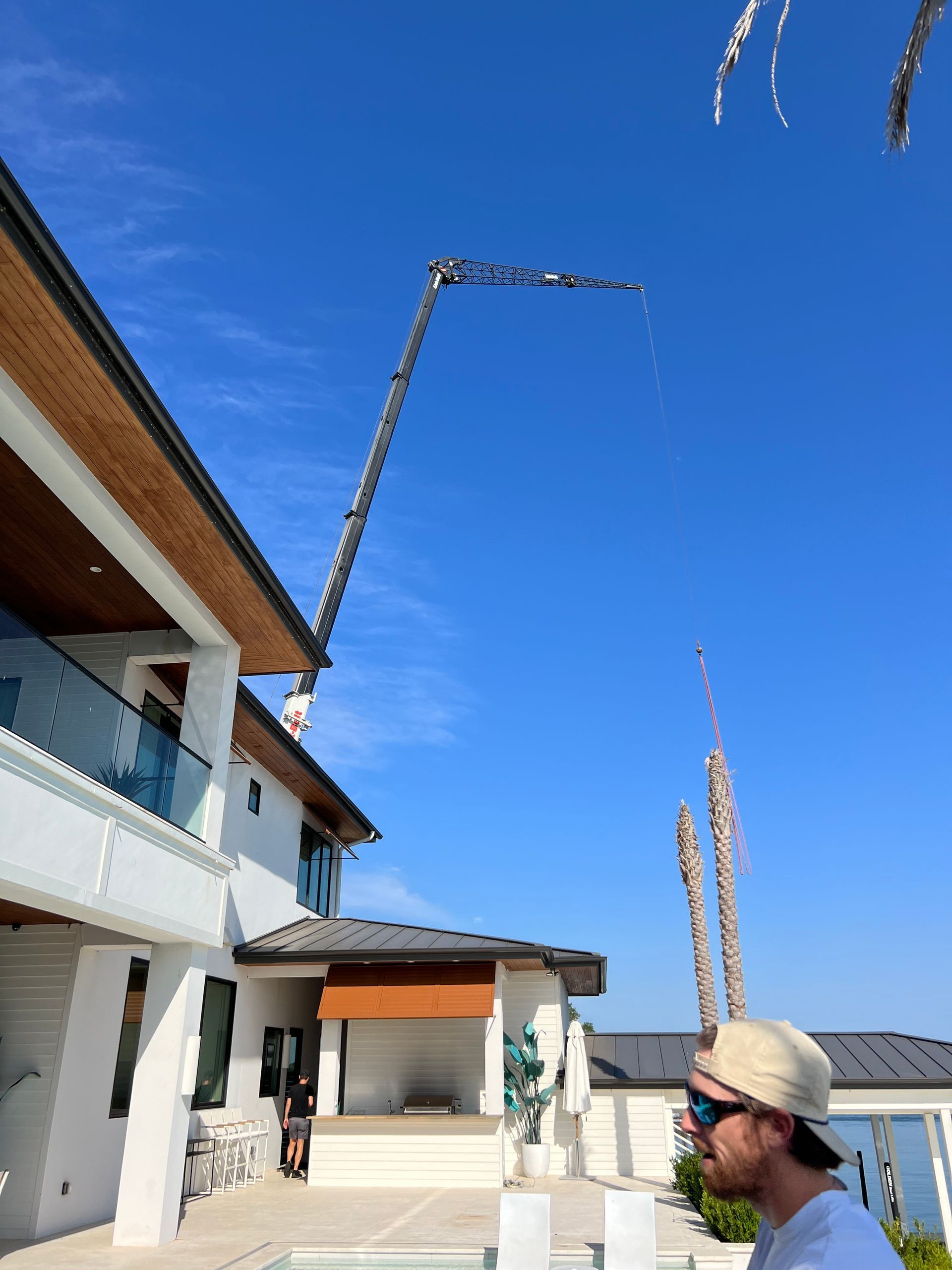 Concrete pump truck over a luxury house. A man watches in the foreground under a blue sky.