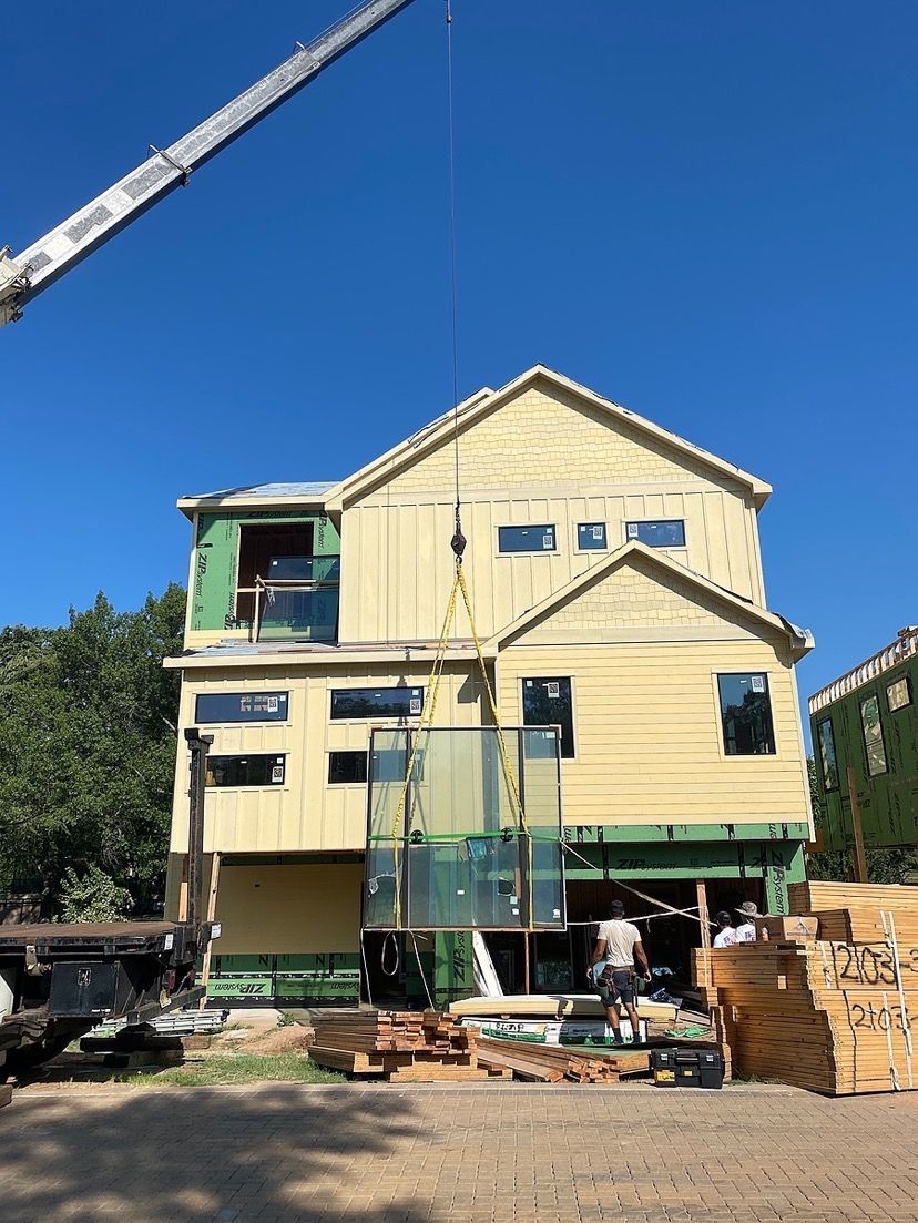 Construction site: crane lifting glass panels onto a two-story house under construction, sunny day.