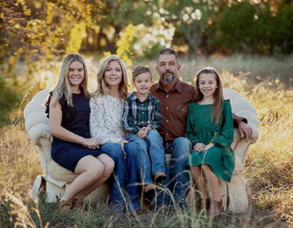 Family in matching pajamas holds framed photo; next to a Christmas tree.