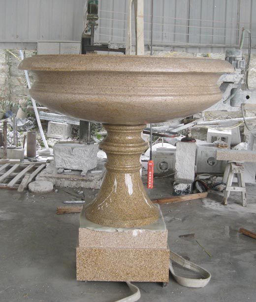 A large stone bowl is sitting on a pedestal in a warehouse.