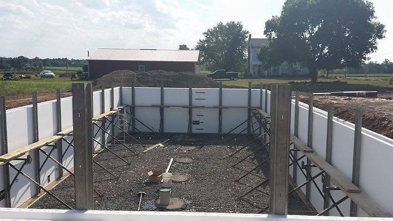 An in-ground foundation under construction with white insulated concrete forms, wooden bracing, and a gravel base.