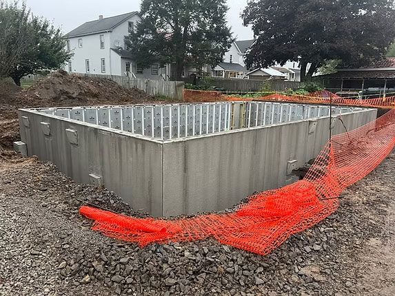 A new concrete foundation for a building under construction, surrounded by orange safety fencing on a gravel lot.