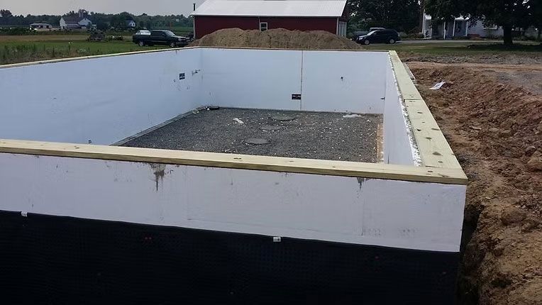 An unfinished foundation with white insulated walls and a gravel base, viewed from an outdoor construction site.