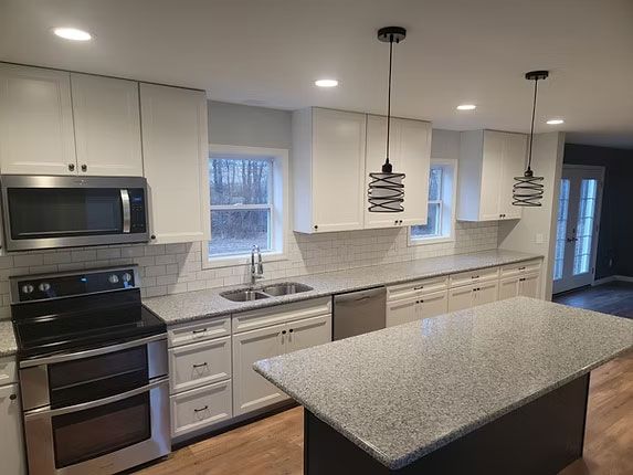 Modern kitchen with white cabinetry, stainless steel appliances, grey granite countertops, and two pendant lights.