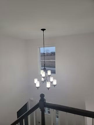 A tiered chandelier with glass shades hangs in a tall stairwell above a dark wooden railing.