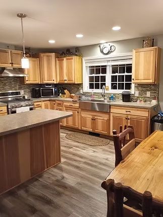 A bright, modern kitchen featuring light wood cabinets, a stainless steel farmhouse sink, an island, and gray flooring.