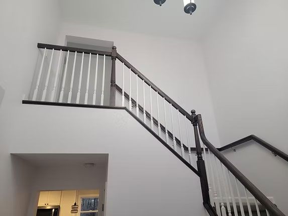 Interior shot of a residential staircase with dark wood handrails and white balusters against plain white walls.
