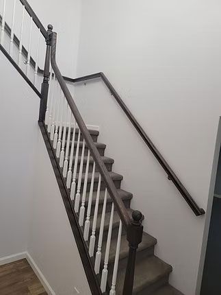 A carpeted staircase with white balusters and a dark wood handrail leading to an upper floor in a white-walled interior.