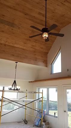 Interior view of a room with a sloped wooden ceiling, a ceiling fan, windows, and metal construction scaffolding.