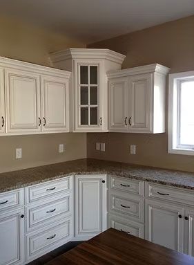 White kitchen cabinets with granite countertops and a corner glass-pane cabinet in a beige-walled room.