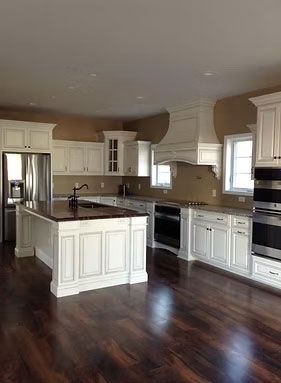 A modern white kitchen with dark wood floors, a center island with a dark countertop, and stainless steel appliances.