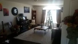 A living room with a coffee table, a white rug, a piano, and a window with curtains and a step ladder in front.