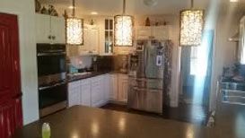 A modern kitchen with white cabinets, stainless steel appliances, three patterned pendant lights, and a red door.