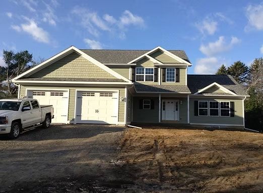 A two-story, sage green house with an attached two-car garage, a white front door, and a white pickup truck parked in front.