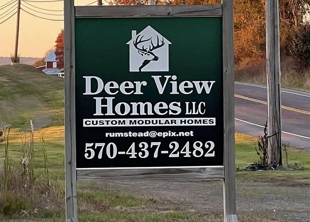 A roadside sign for "Deer View Homes LLC," featuring a deer logo and contact information on a green background.