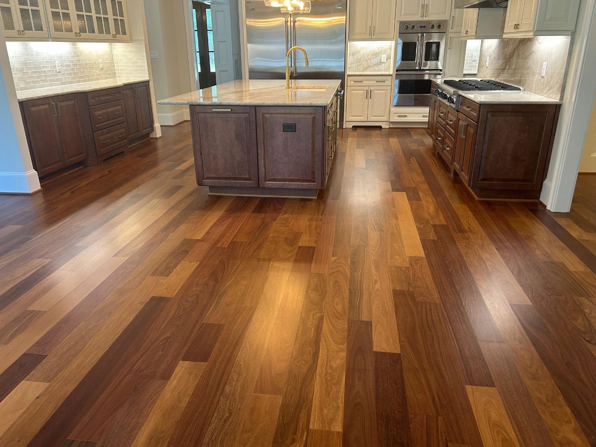 A modern kitchen with brown wooden cabinets, a large central island, and polished hardwood flooring.