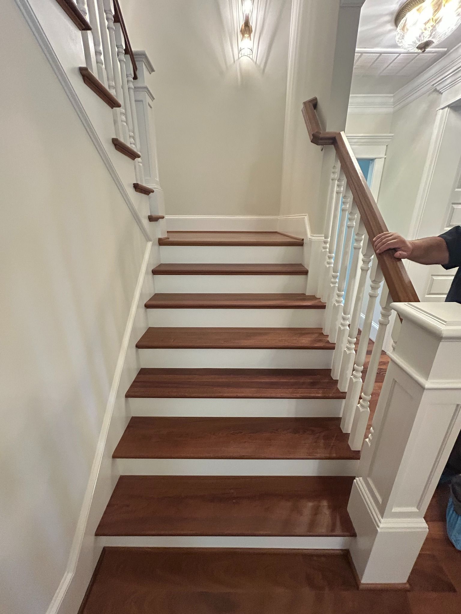 A wooden staircase with white risers, leading upward with white balusters and a dark handrail in a bright home interior.