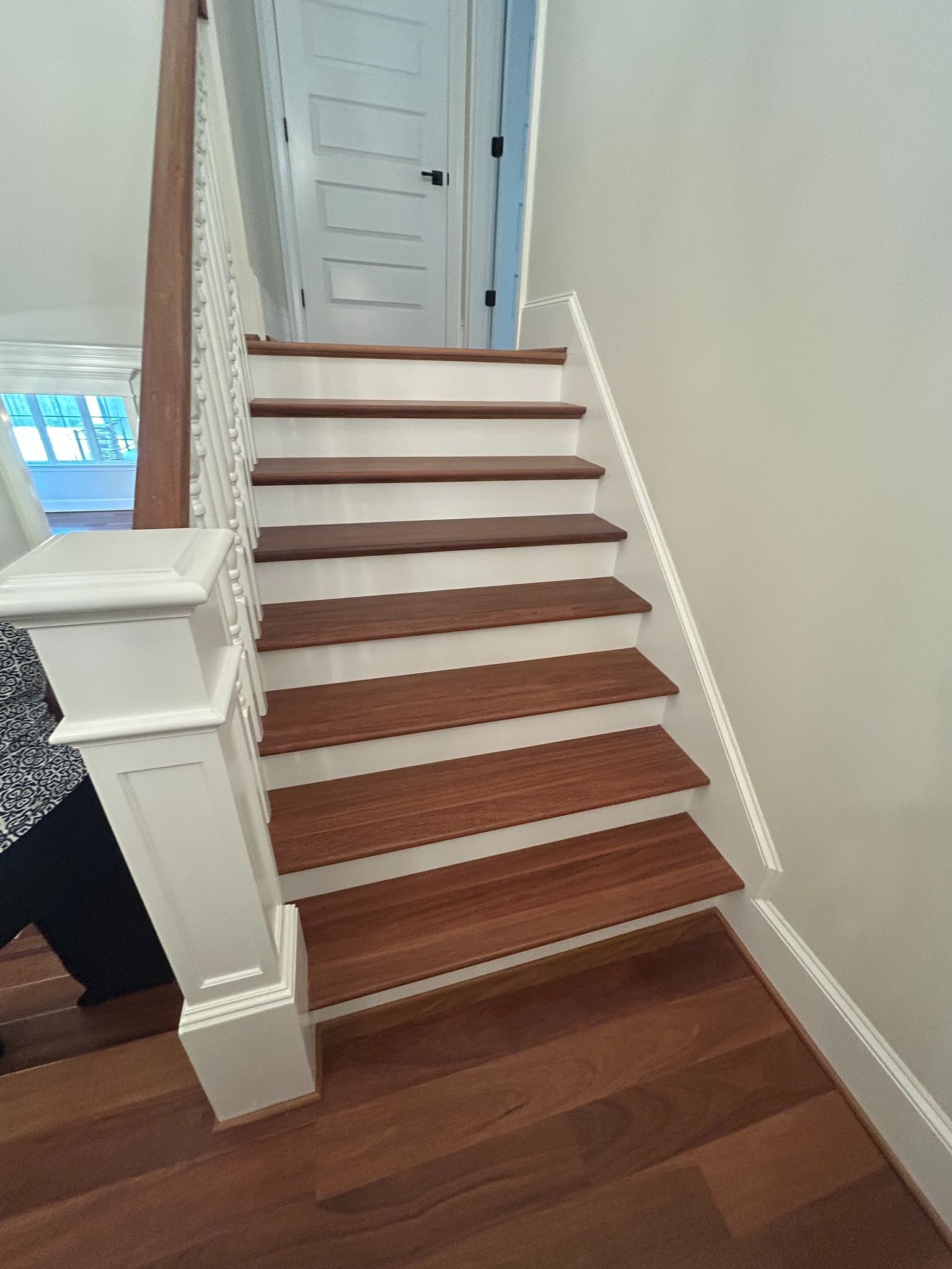 A staircase with dark wood treads and white risers, featuring a white decorative newel post in the foreground.