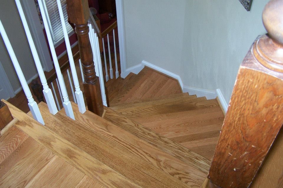 A high-angle view looking down a wooden staircase with white balusters and a dark wood handrail.