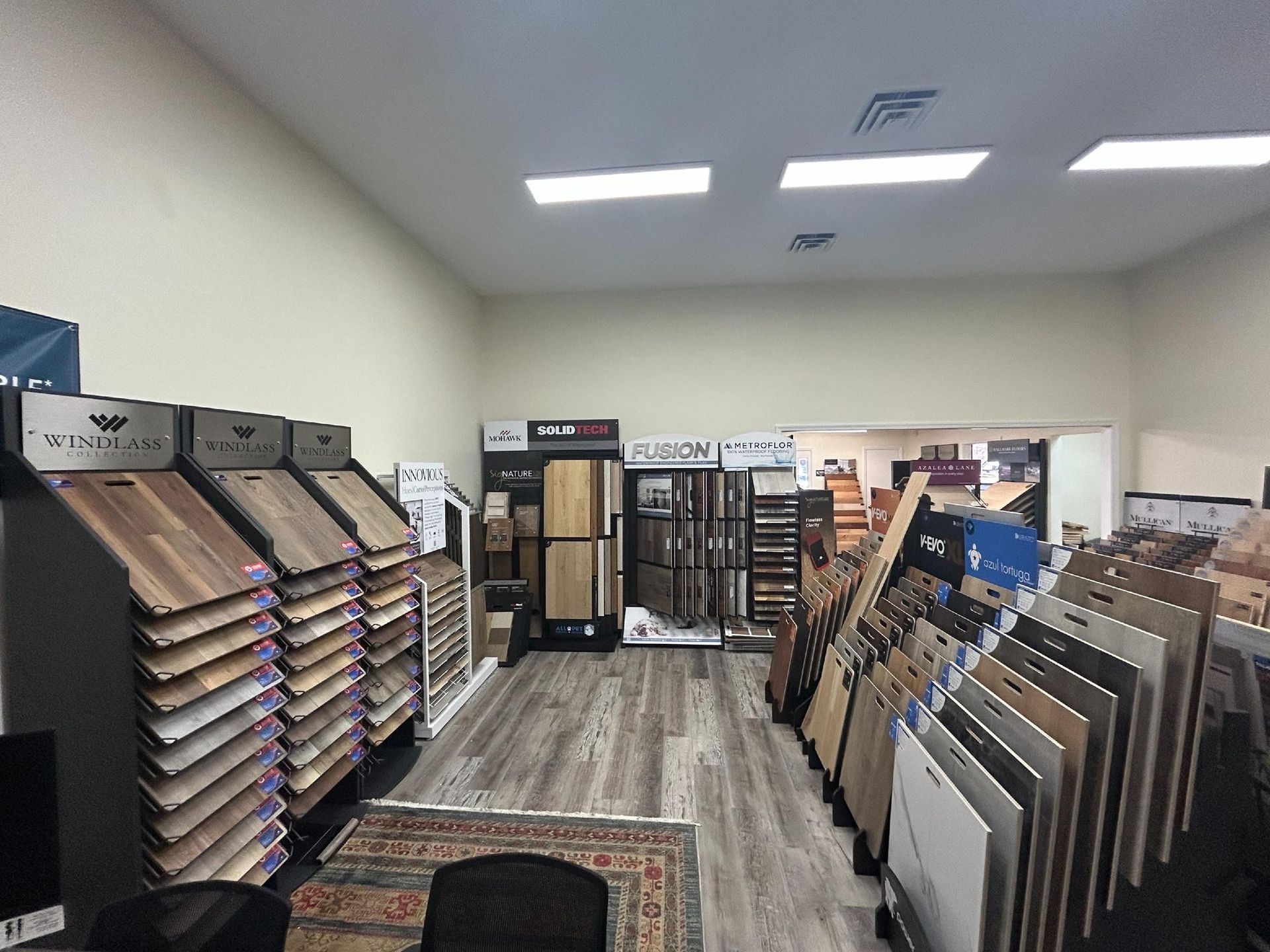 A showroom interior features rows of flooring samples and wood panel displays arranged on shelves across a laminate floor.
