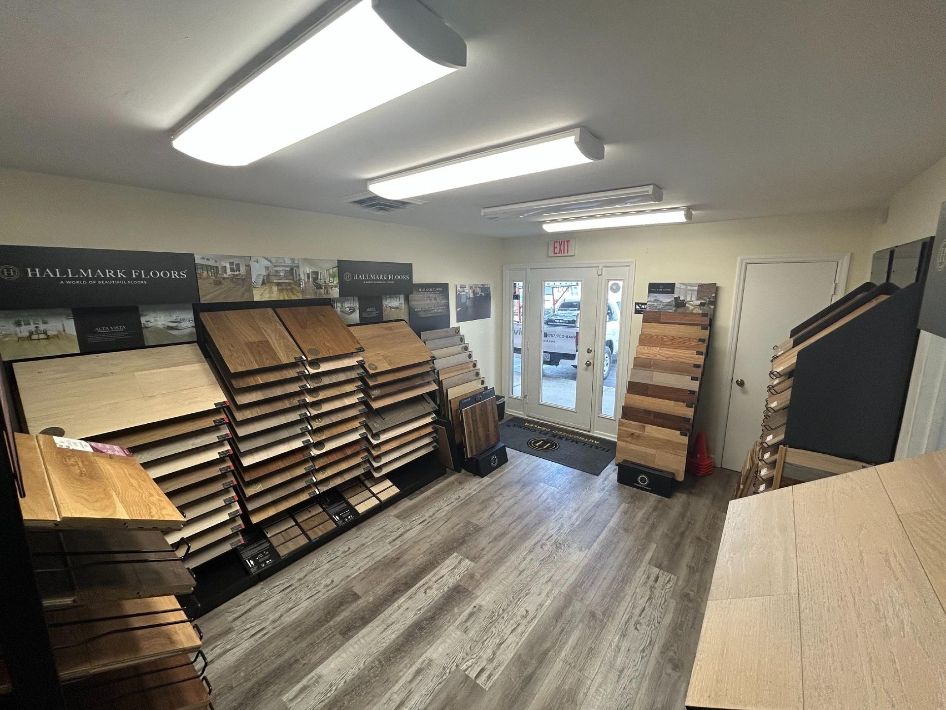 A showroom with various wood and laminate flooring samples displayed on racks and a light wood-look floor.