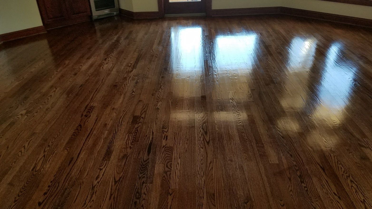 A high-angle view of a freshly finished, glossy dark brown hardwood floor with bright light reflections.