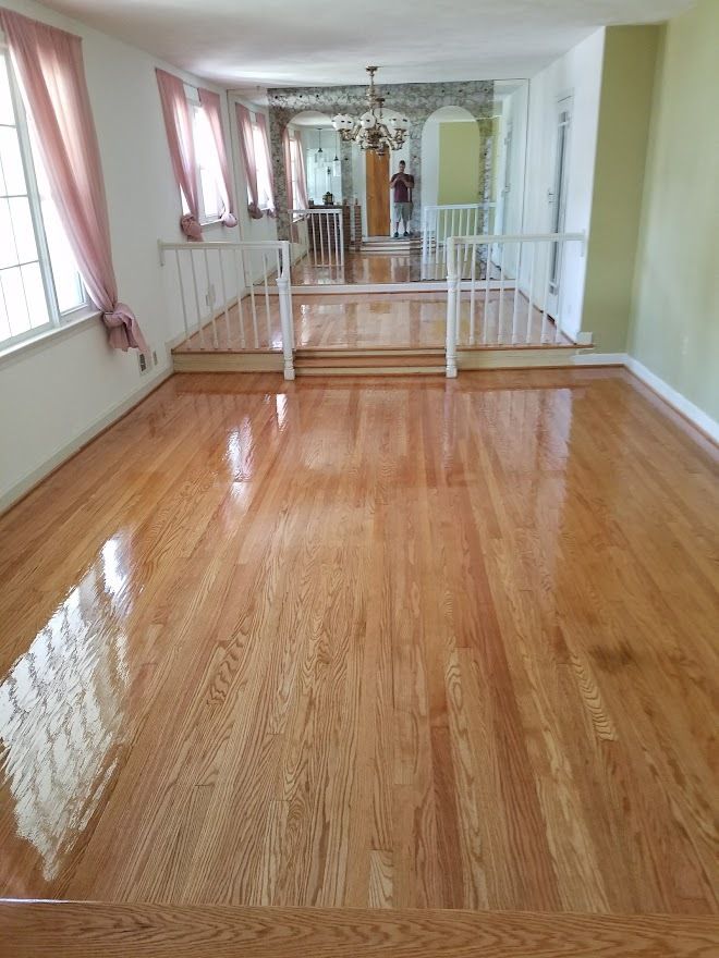A spacious room with polished light-wood floors, featuring a slightly raised level in the back with white railings.