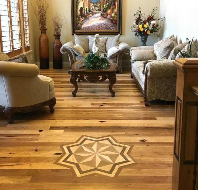 A living room with light wood floors featuring a star-shaped inlay, beige furniture, a coffee table, and wall art.
