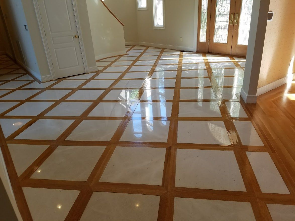 Foyer flooring featuring a grid pattern of polished white square tiles framed by warm-toned wooden borders.