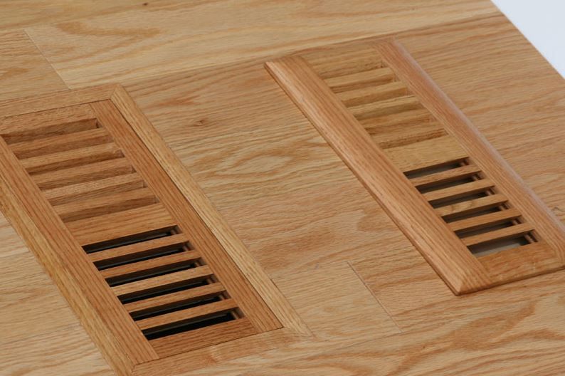Two wooden floor vents with horizontal slats installed flush in a light oak hardwood floor.
