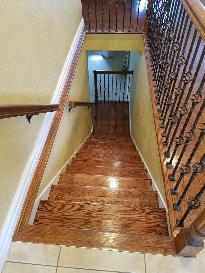A top-down view of a wooden staircase with dark metal railings, leading down to a landing with a window.