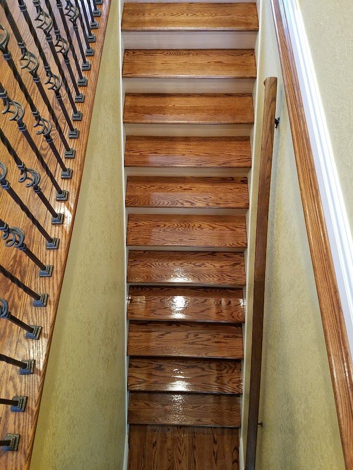 A straight wooden staircase with dark metal railings on the left and a handrail on the right against textured yellow walls.