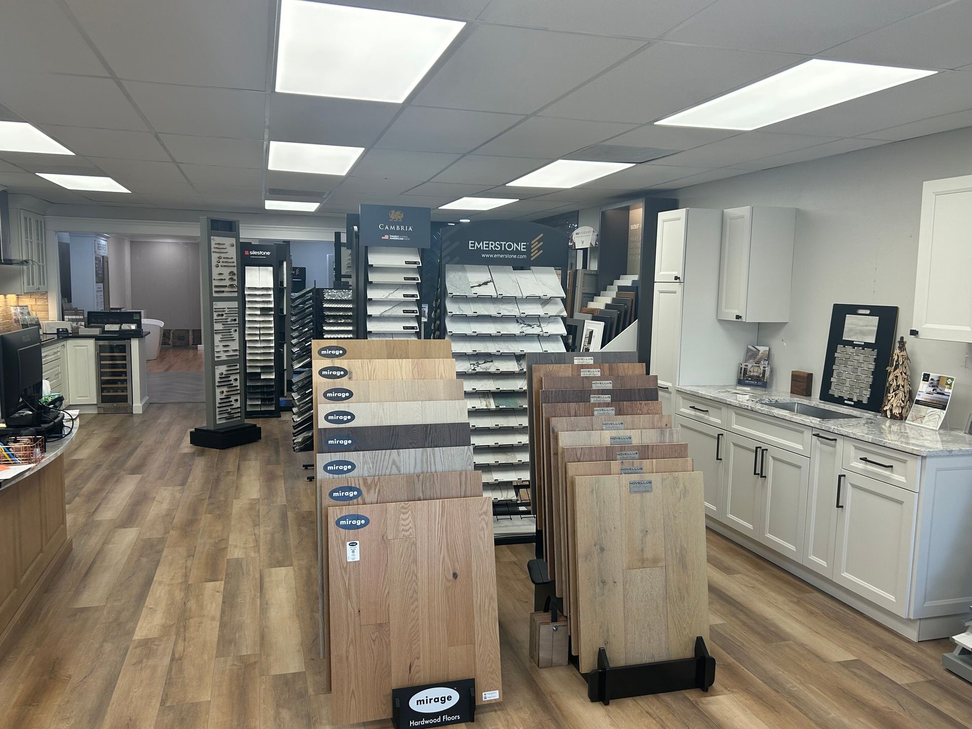A showroom featuring wood flooring samples, kitchen cabinet displays, and tiled walls under bright ceiling lights.