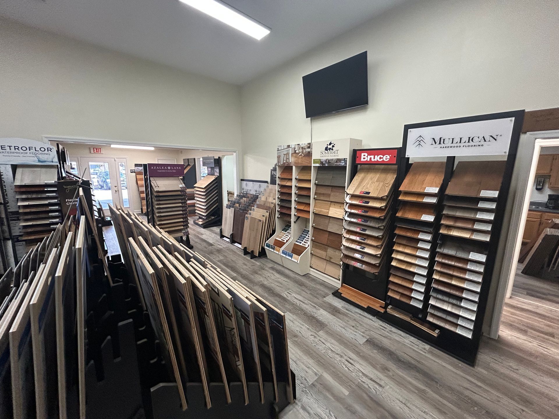 An interior view of a flooring showroom featuring rows of wood, tile, and vinyl sample displays under recessed lighting.