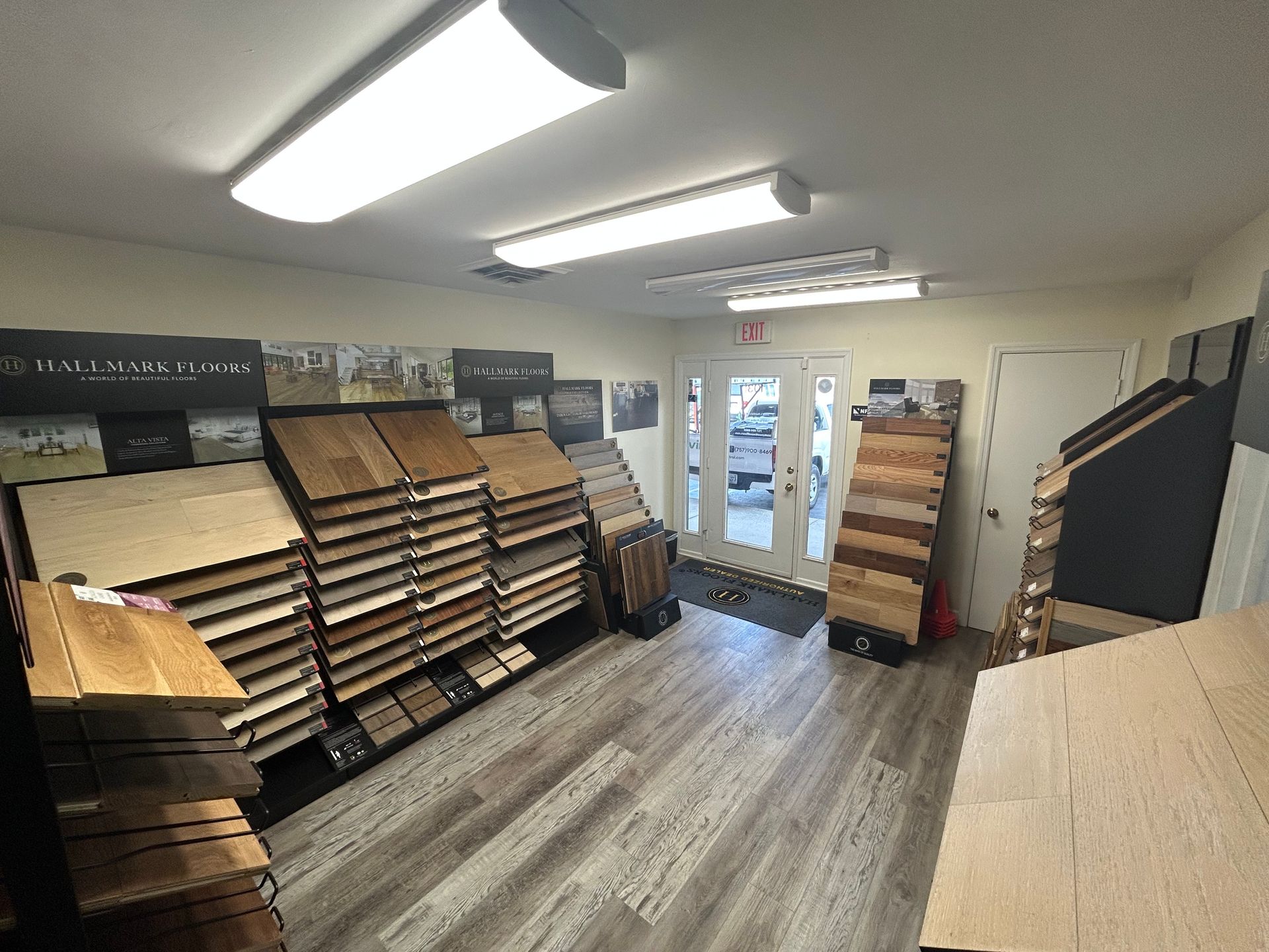 A flooring showroom interior with wood-toned sample racks arranged along the walls and a light wood-plank floor.