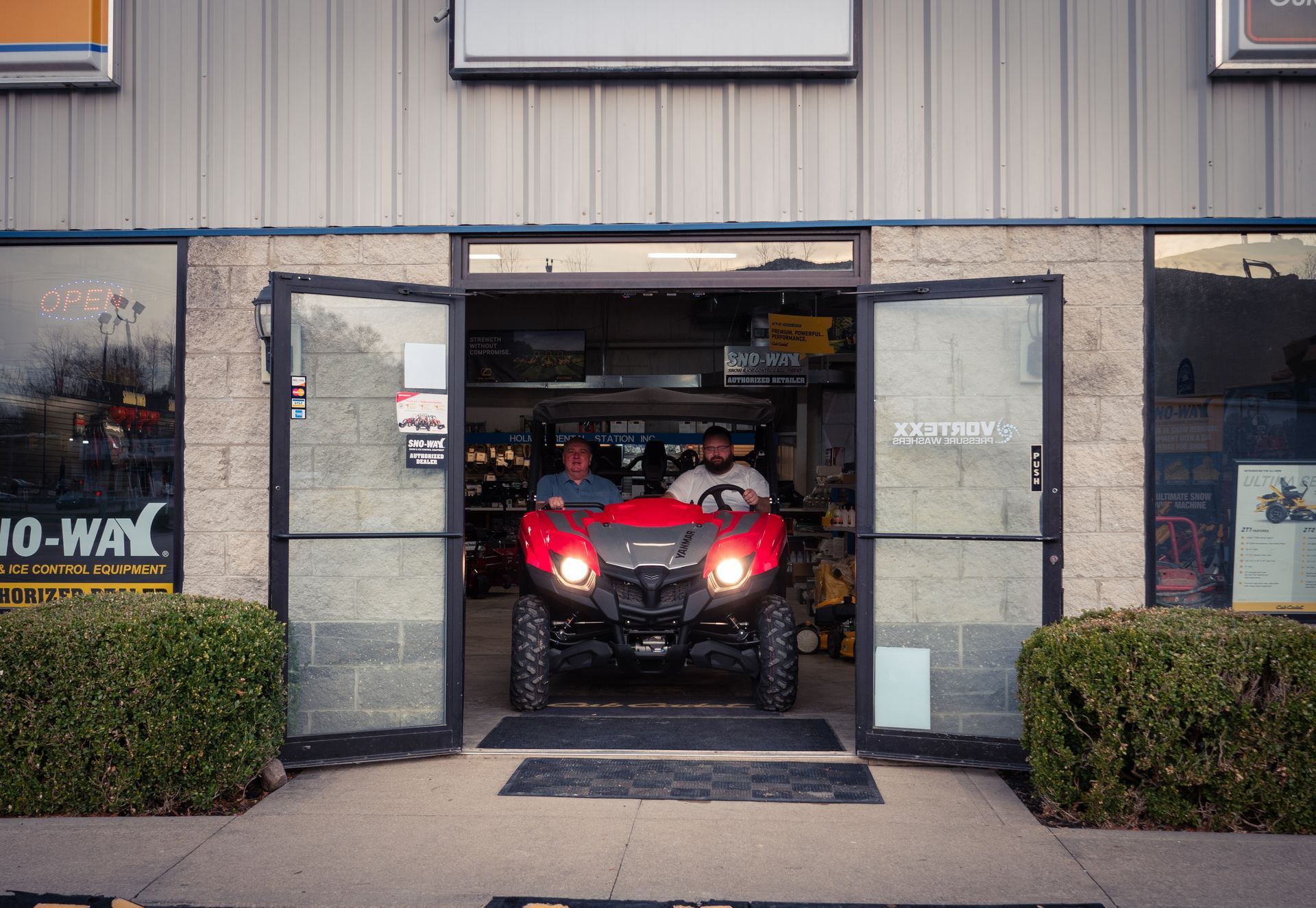 Two men are driving a red atv through the doors of a building