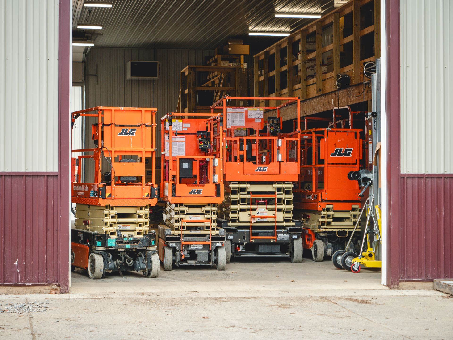 A row of orange scissor lifts are parked in a garage.