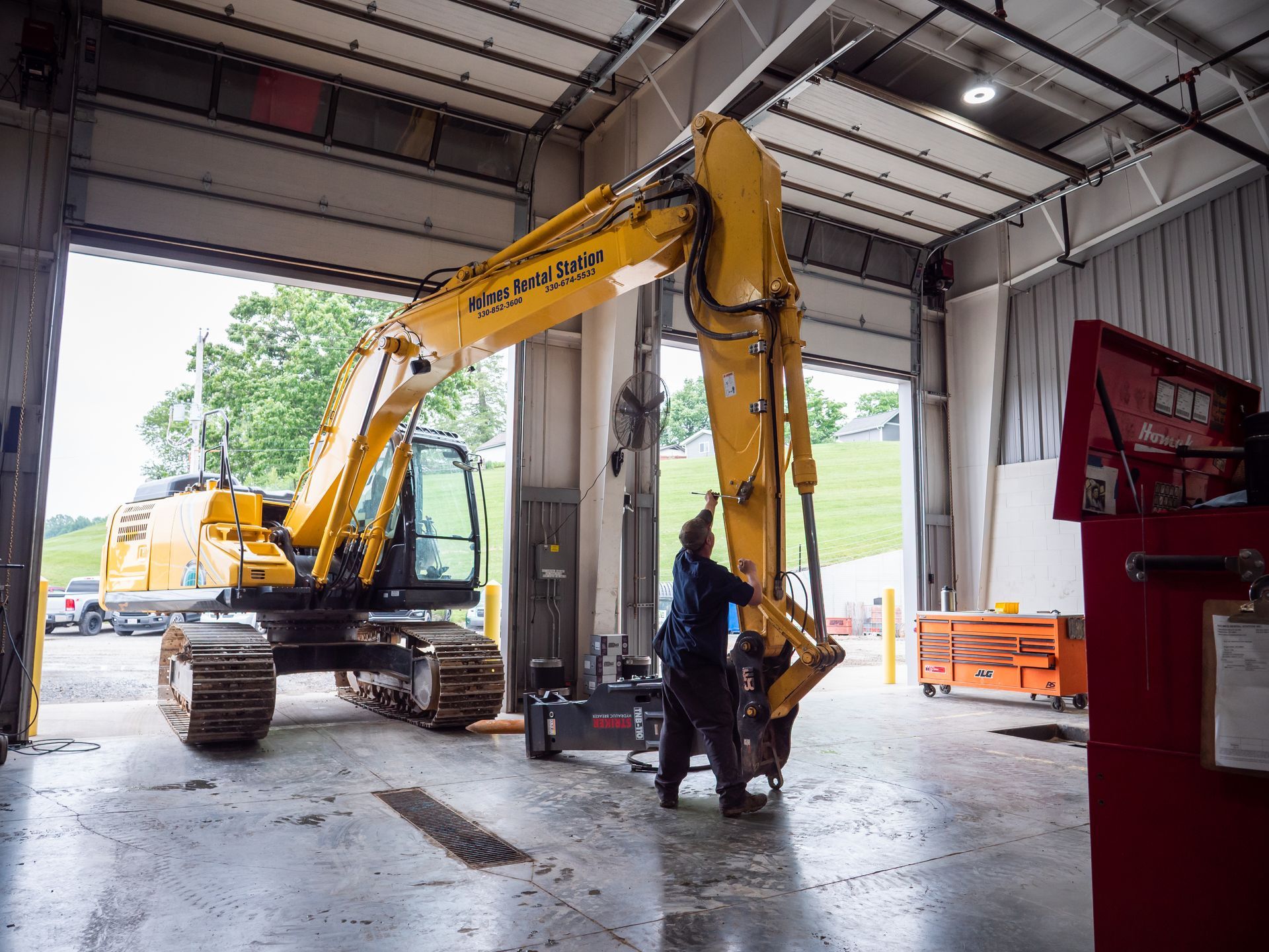 A man is working on a yellow excavator in a garage.
